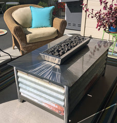 A hand brushed stainless steel rectangular IMPACT fire table with salvaged corrugated side panels burning natural gas.
