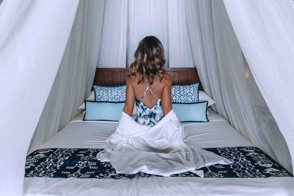 This Island Life sitting on the bed of her beach bungalow in Bawah Island wearing the London Print Slip and Ivory Silk Cotton robe