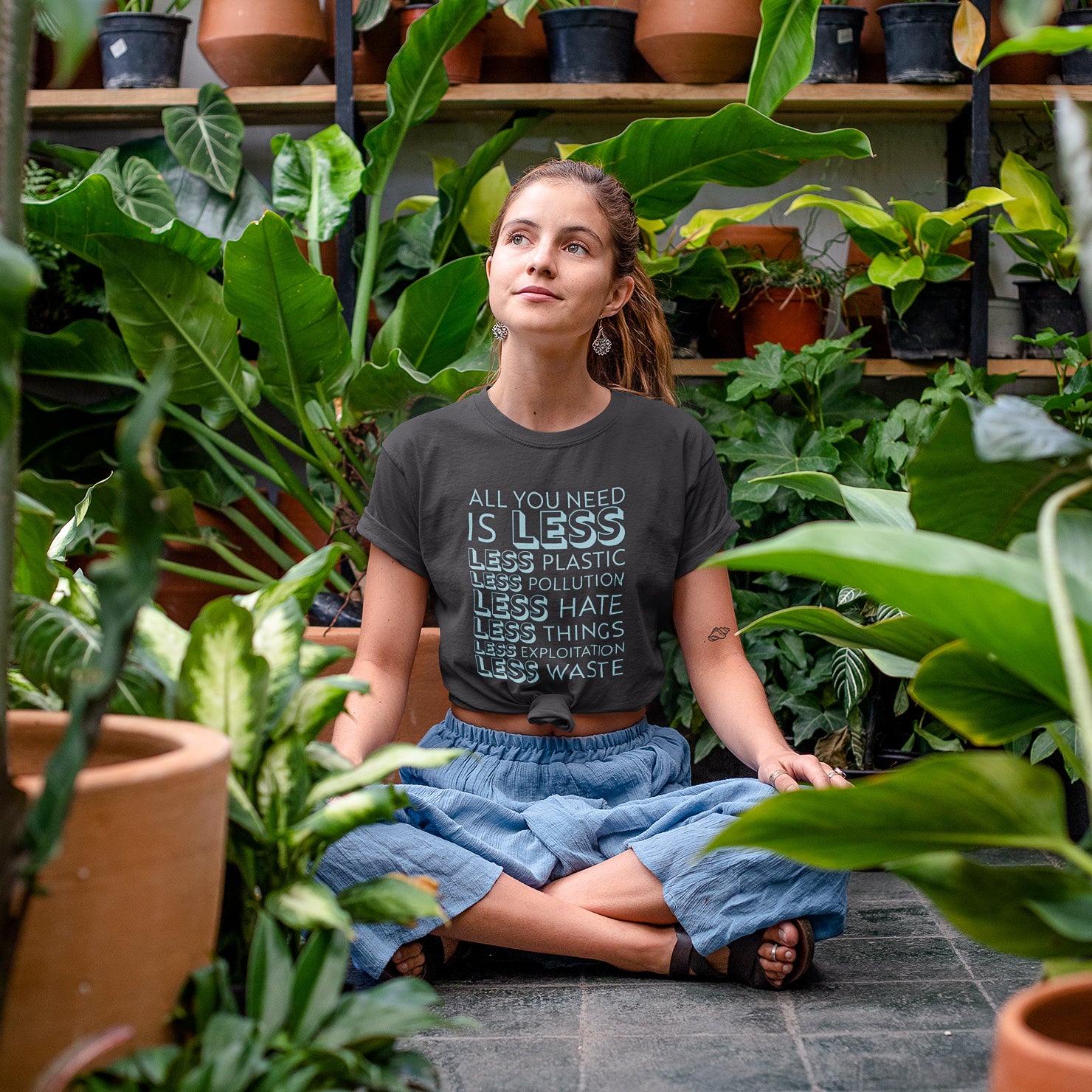 girl in greenhouse surrounded by plants wearing gray getpinkfit "All You Need Is Less" shirt - getpinkfit donated 10% of profits to non-profit organizations - ethically and sustainably made clothing