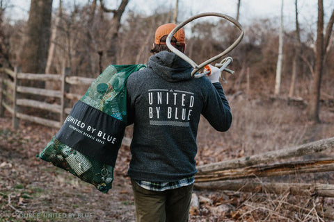 United By Blue Team Member Wearing a Jacket and Carrying a Bag of Trash During a Cleanup - sweetsherriloudesigns Blog - 7 Eco-friendly Companies That Give Back To Our Planet