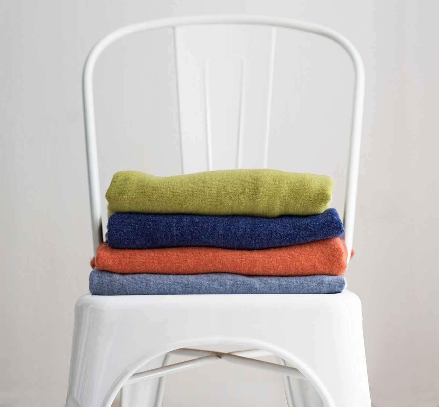Folder-cashmere-jumpers-stacked-on-a-white-chair-in-front-of-a-white-wall