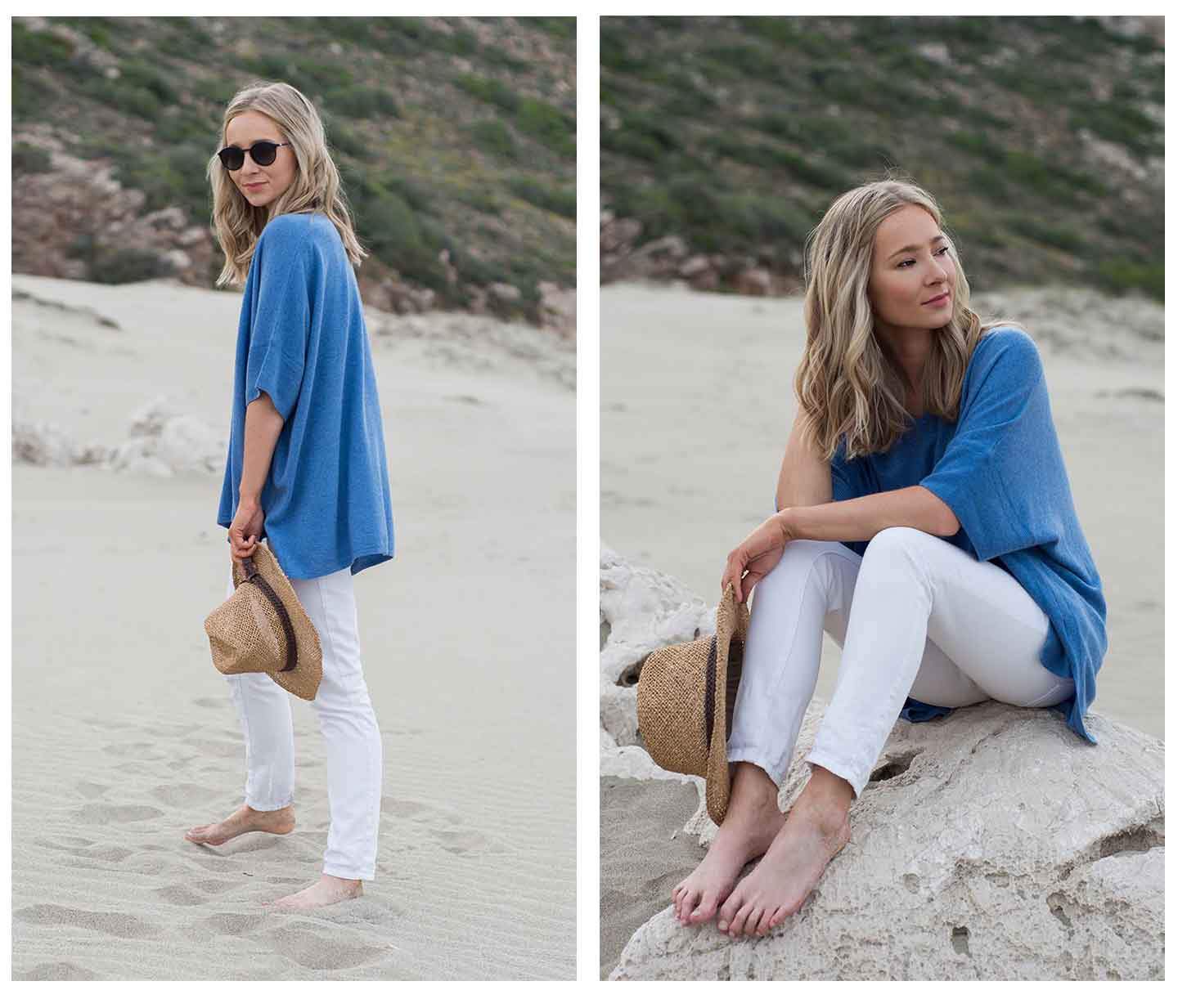 woman-on-beach-wearing-a-blue-cashmere-kimono-jumper-with-white-jeans-sunglasses-and-a-straw-hat