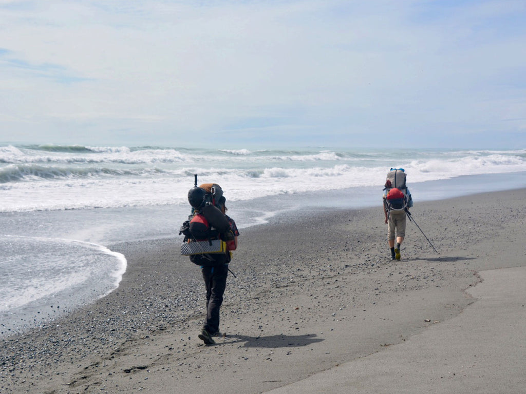Ultralight backpackers walk along a beach
