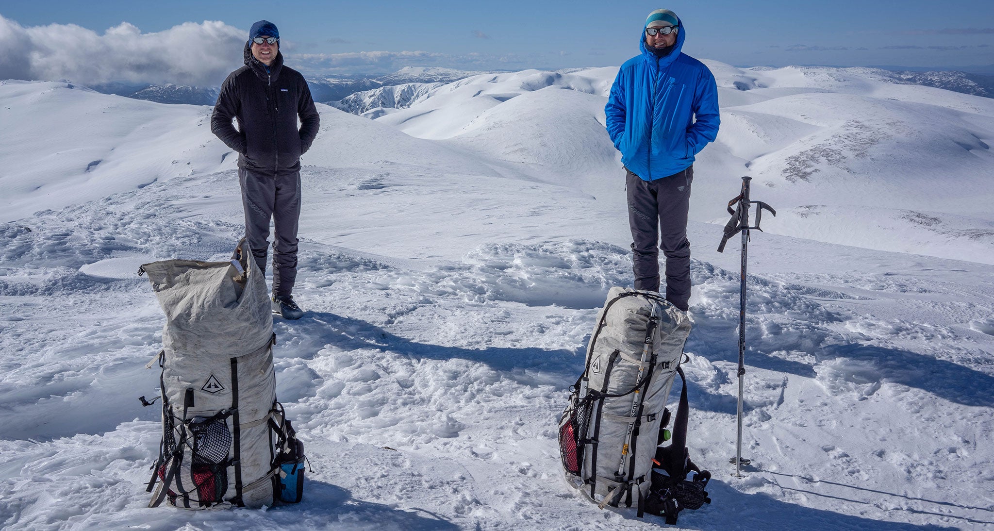 Two hikers pose in the snow with ultralight backpacks