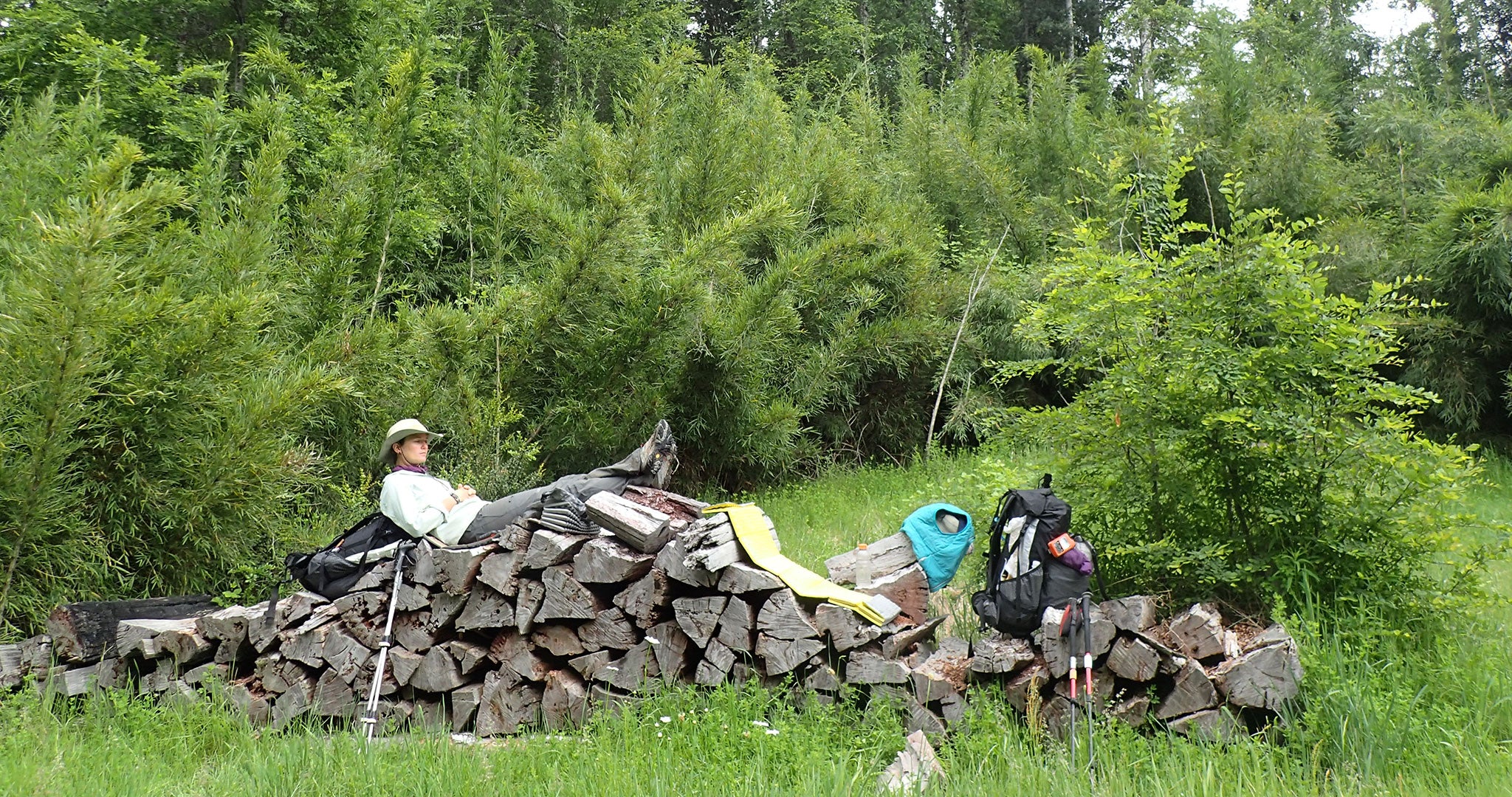 Ultralight backpacker resting atop a wood pile.