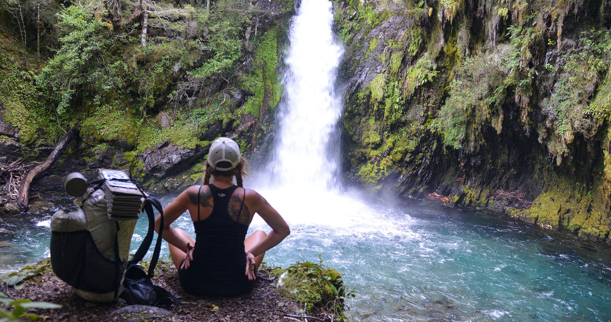 Ashley Hill sitting with ultralight backpack overlooking a waterfall