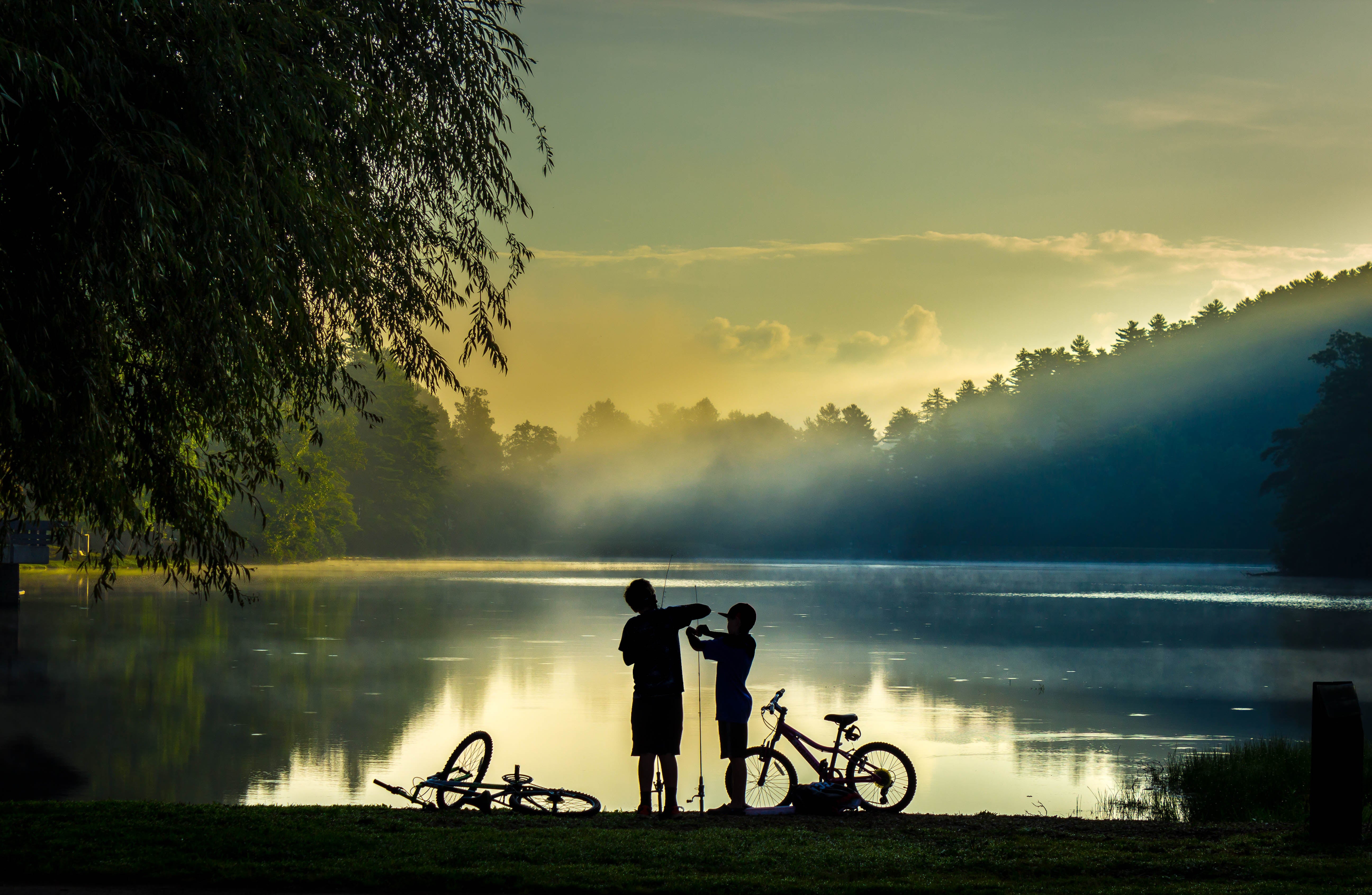 Silhouette of Two Kids on The Lake with Fishing Rods and Bikes