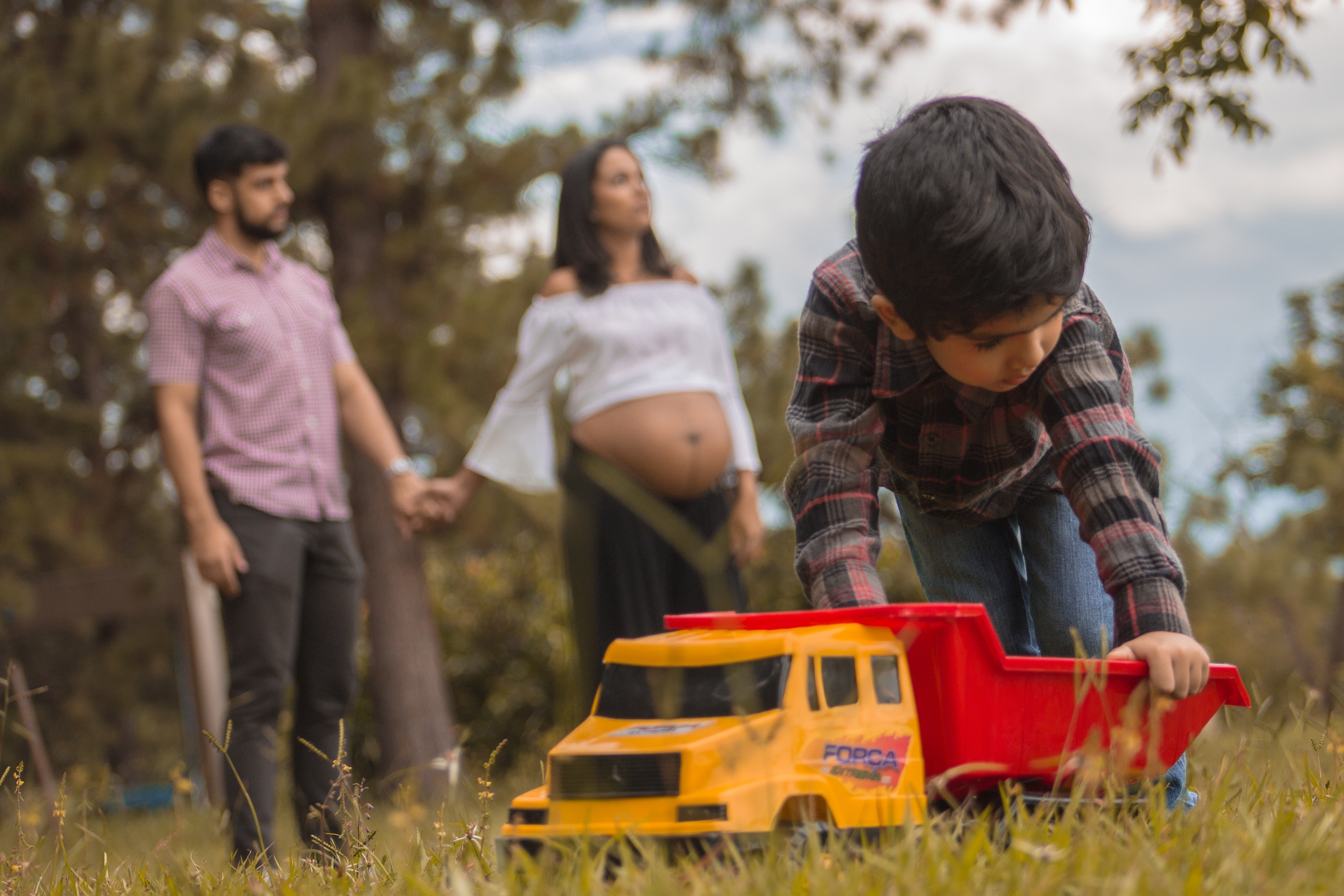 Boy Playing with Toy Truck with Father and Pregnant Mother in Background