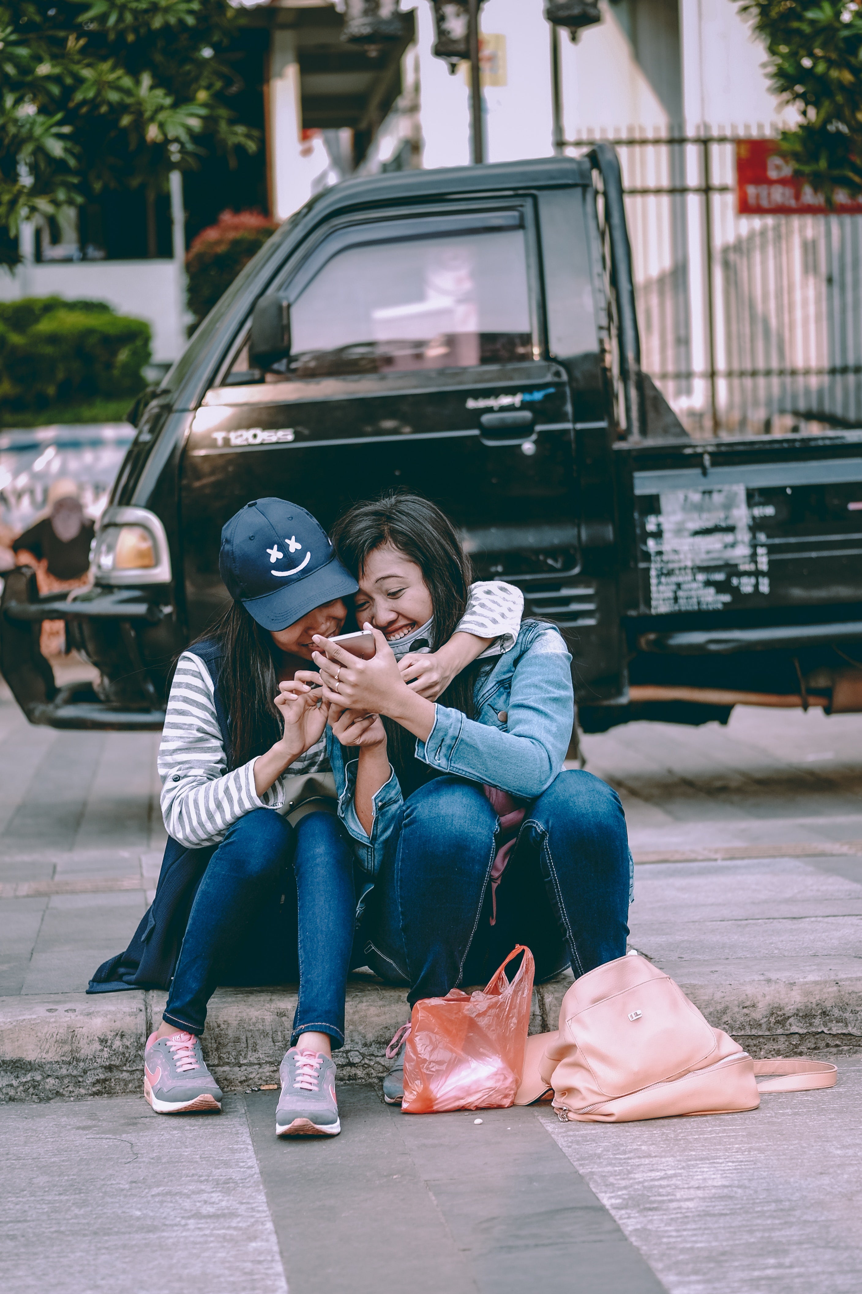 Two Teenagers Sitting on Curb Outside Laughing at Their iPhone - Sibling Photo Idea