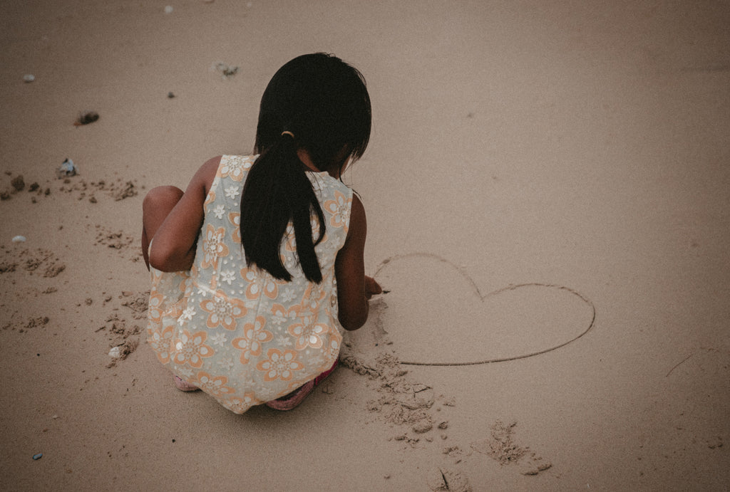 Little girl drawing a heart in the sand at the beach