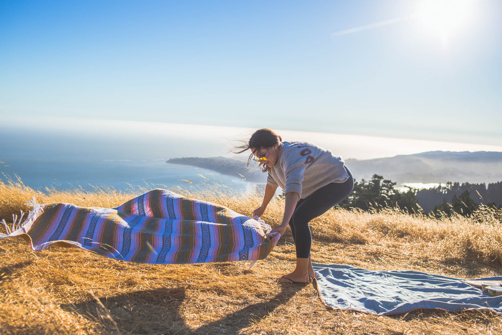 Candid photo of woman laying out a blanket in the wind with the ocean in the background