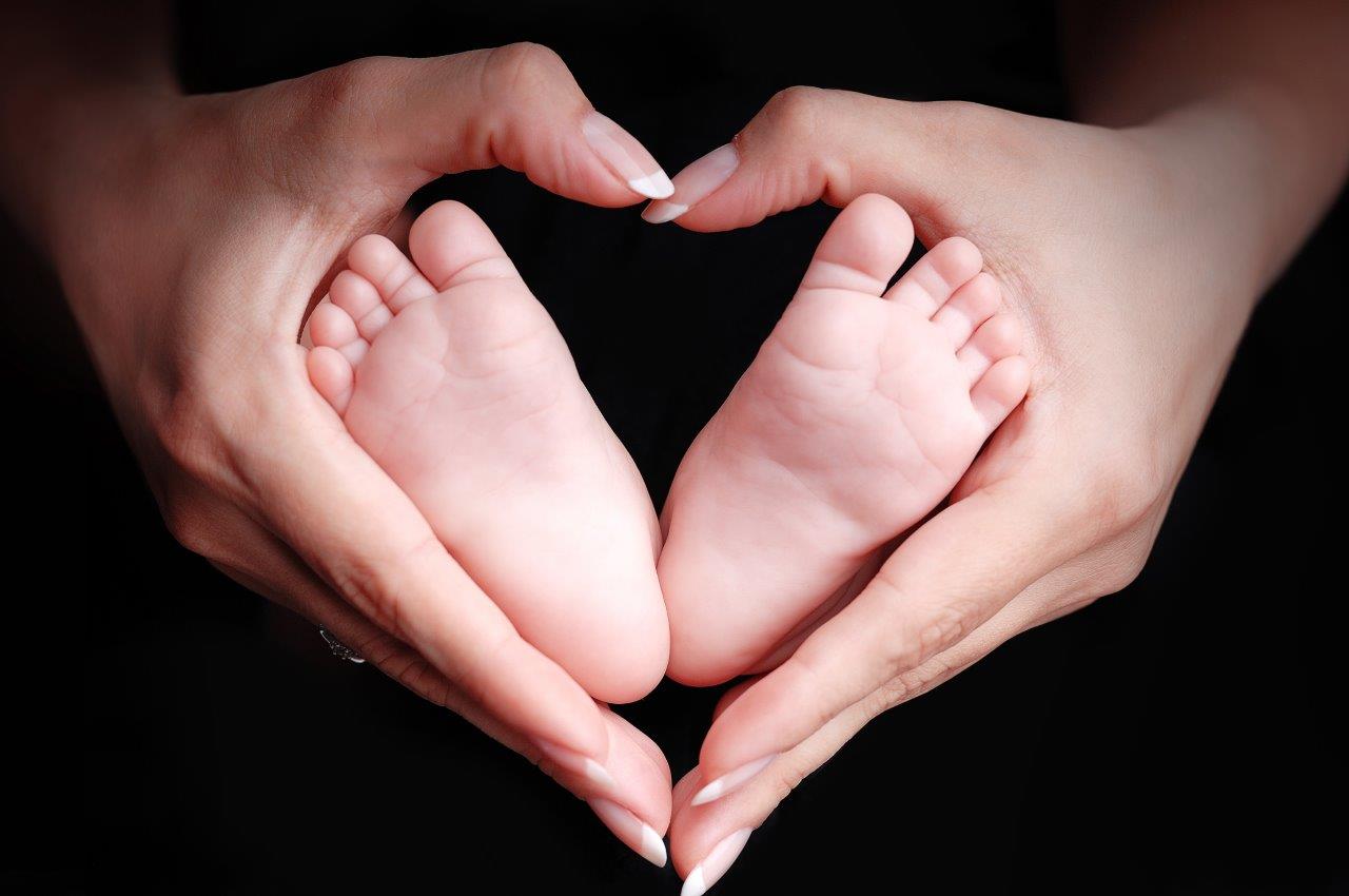 Mother's hands framing baby's feet in the shape of a heart