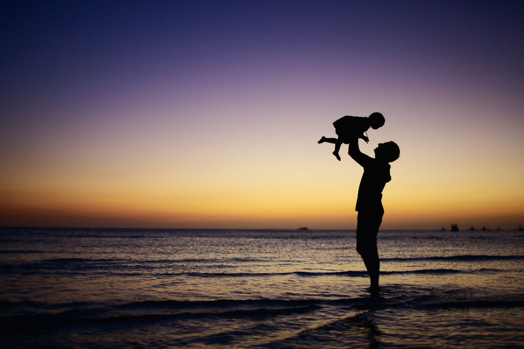 Silhouette of adult and child at the beach at sunset