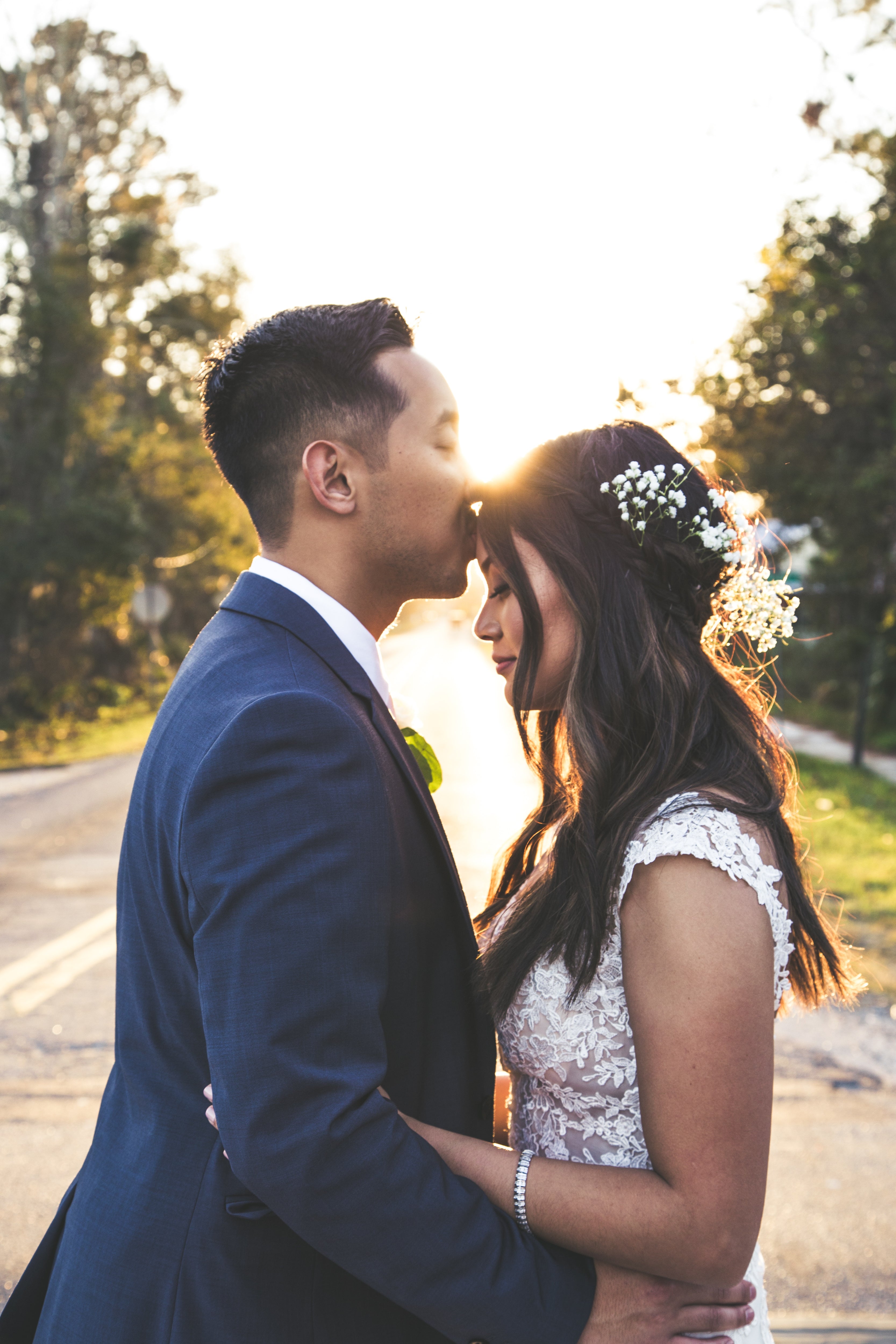Groom kissing bride on forehead with beautiful backlighting by sun