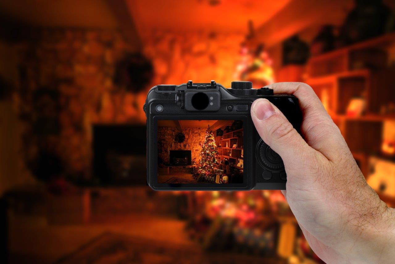 Hand holding a DSLR camera photographing a low-light holiday scene of a Christmas tree