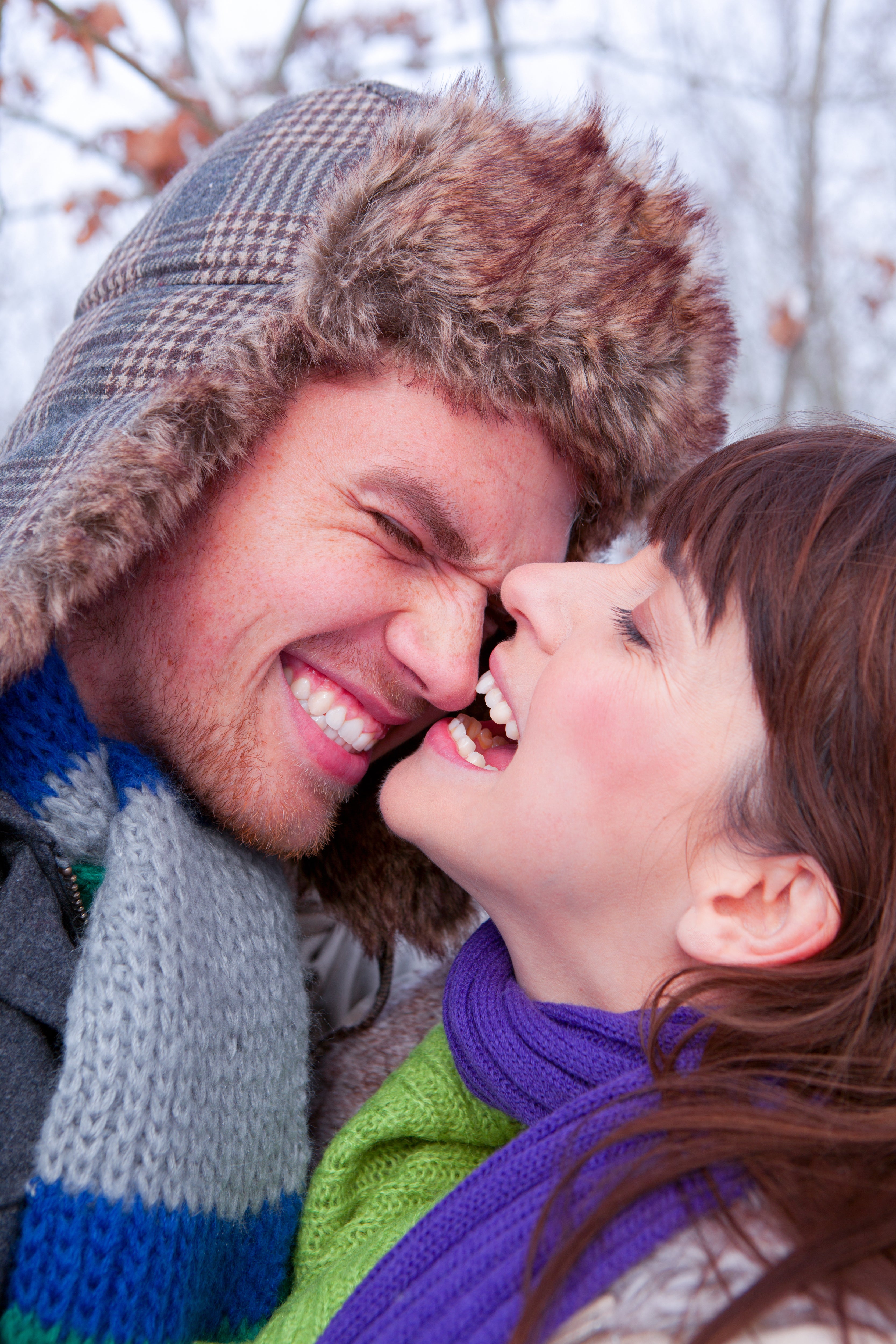 Outdoor winter candid photo of happy man and woman as she playfully bites his nose