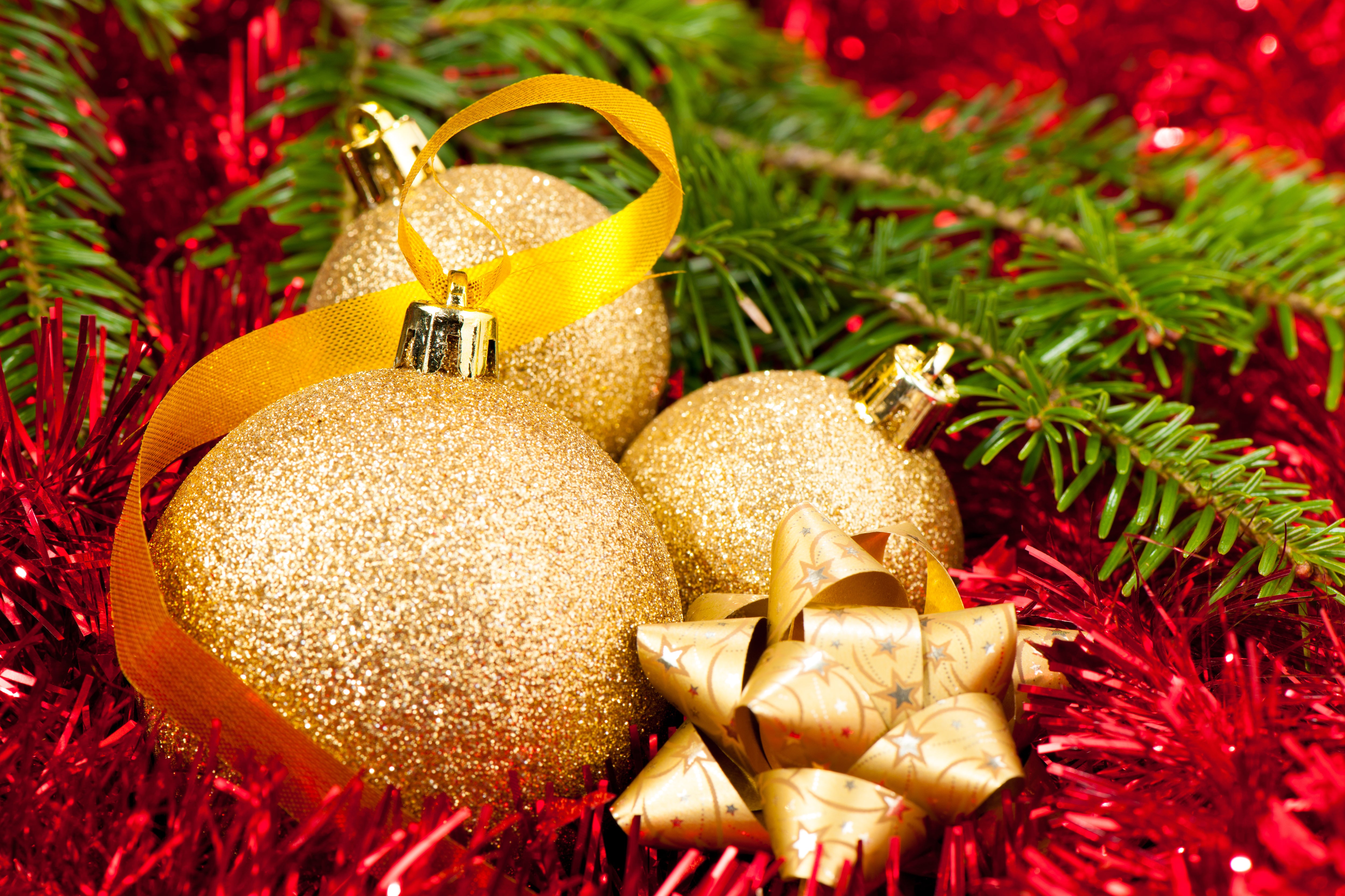 Close-up of gold Christmas decorations with red garland and pine in the background