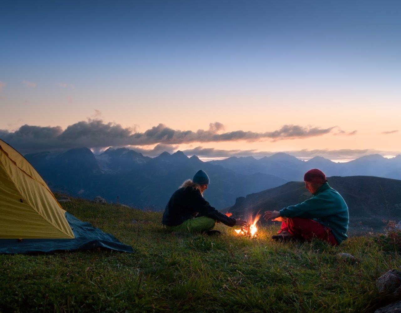 Two people tent camping in the mountains at night with a campfire