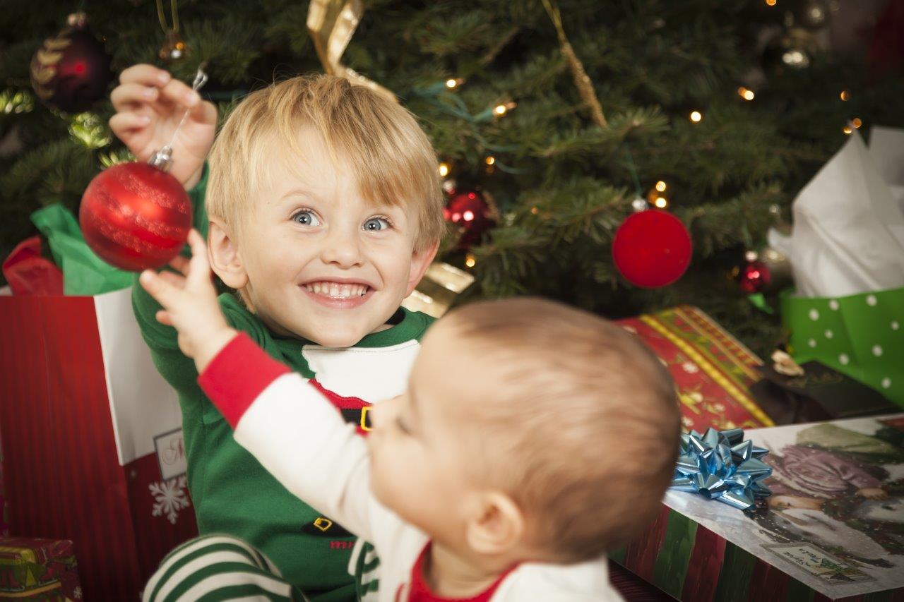 Holiday photo of an excited little boy holding a Christmas decoration away from his little sister