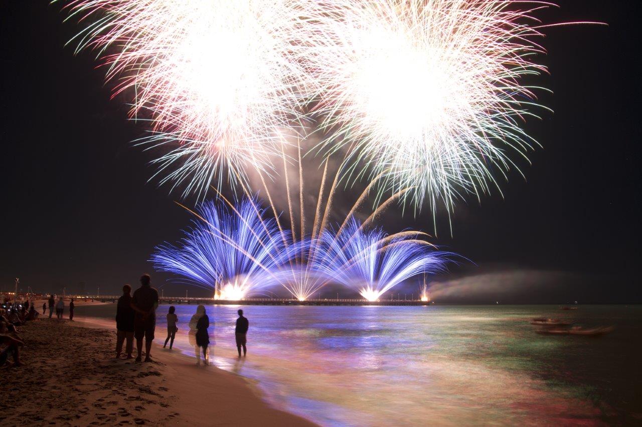 People on the beach at night with fireworks in the background