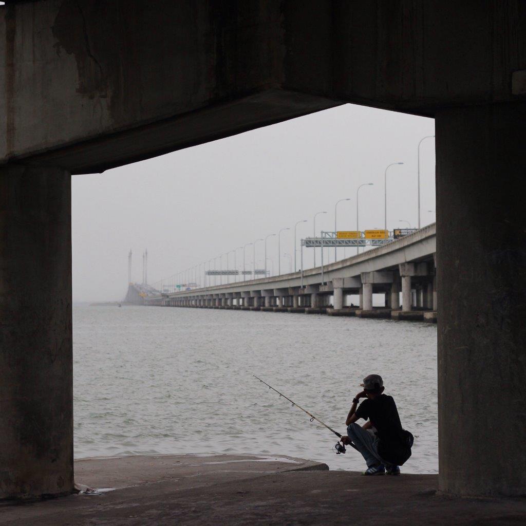 Person fishing under a bridge on an overcast day, an example of creative compositional framing