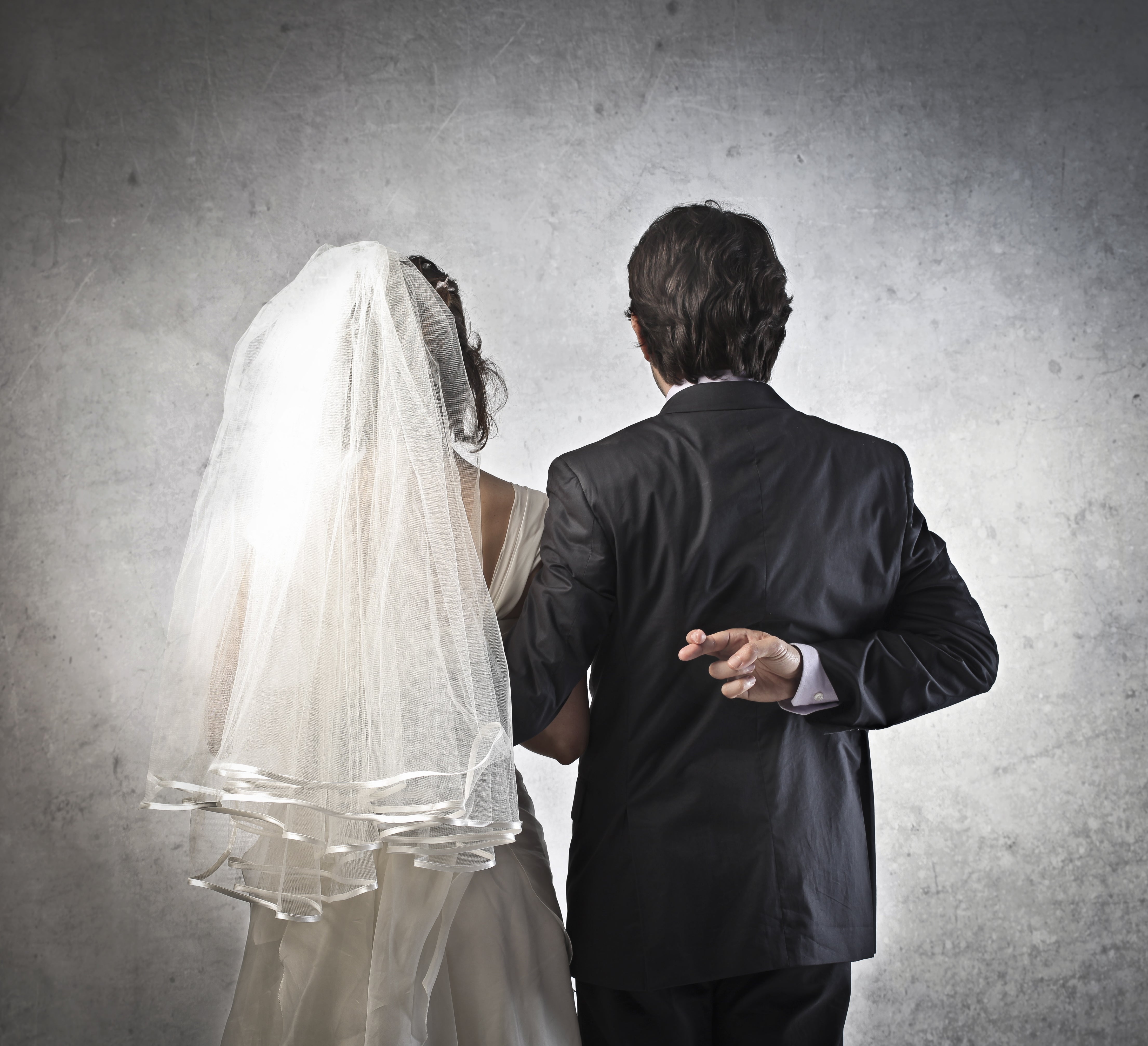 Funny wedding photo of groom crossing his fingers behind his back as he gets married