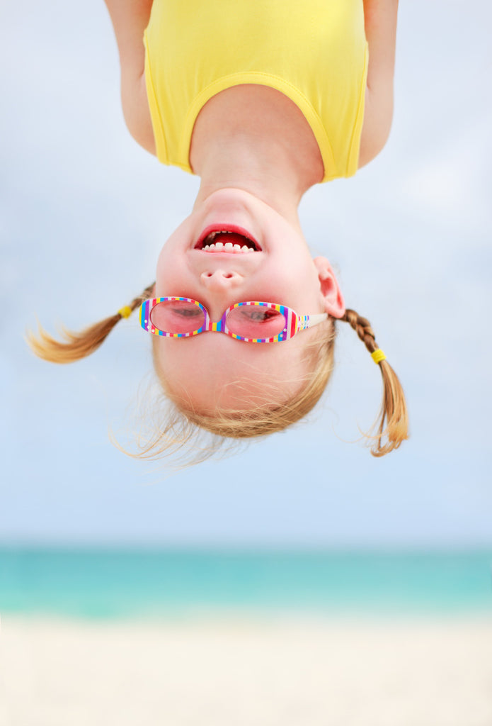Happy little girl hanging upside-down at the beach with ocean in the background
