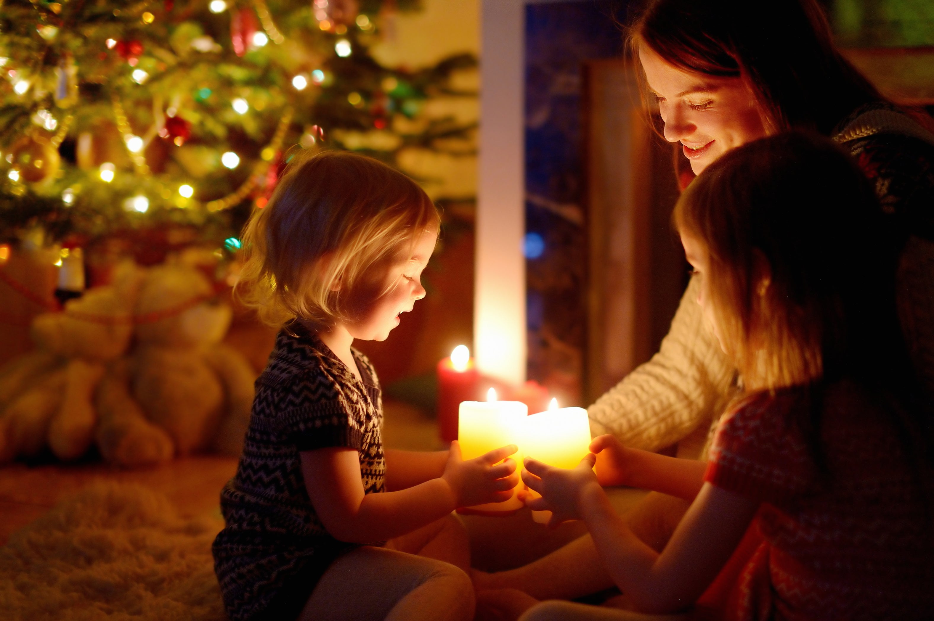 Woman and children holding lit candles in front of the Christmas tree at night - holiday photography example