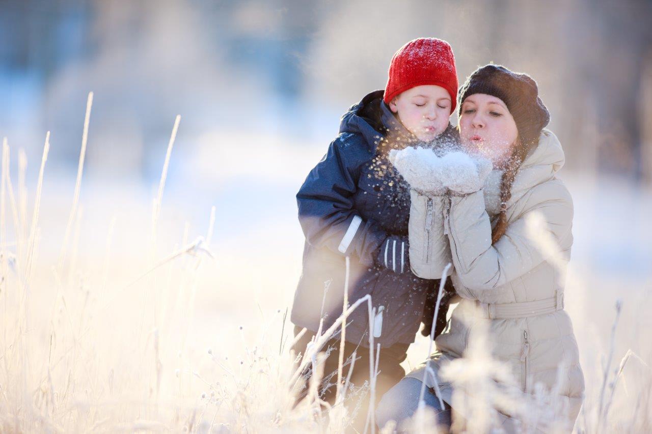 Holiday photo of a mother and child outside blowing snow from their mittens