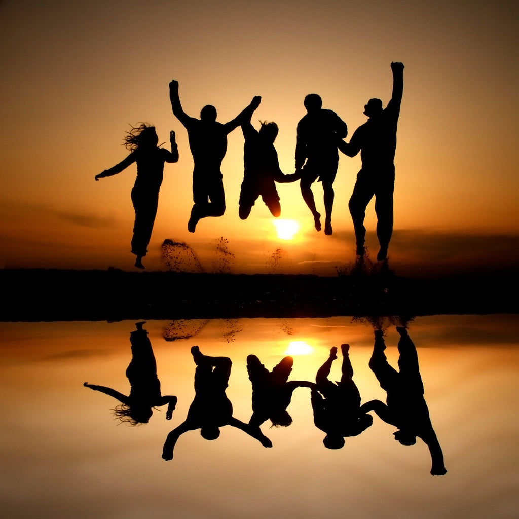 Silhouette photo of a group of friends jumping in the air at the beach having fun at sunset