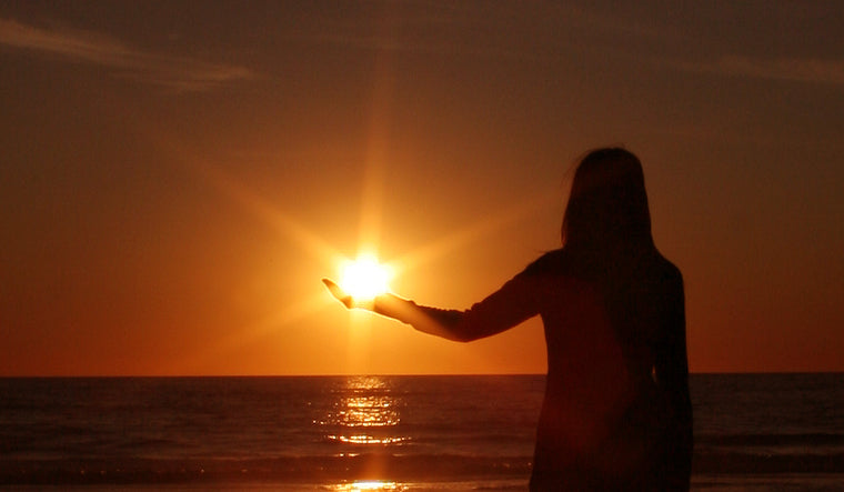 Forced perspective photo of a person holding the sun in their hand during a sunset