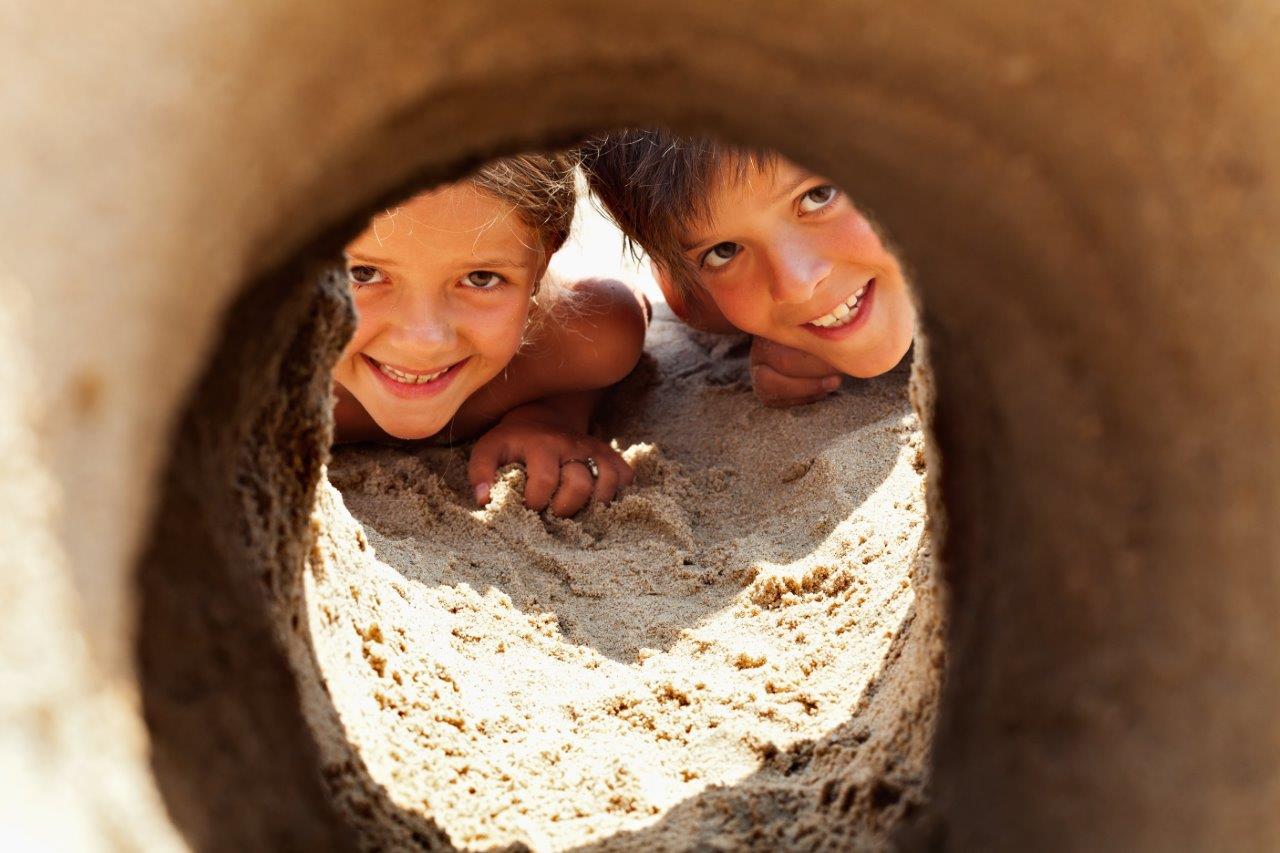 Portrait of children at the beach looking through a hole in the sand