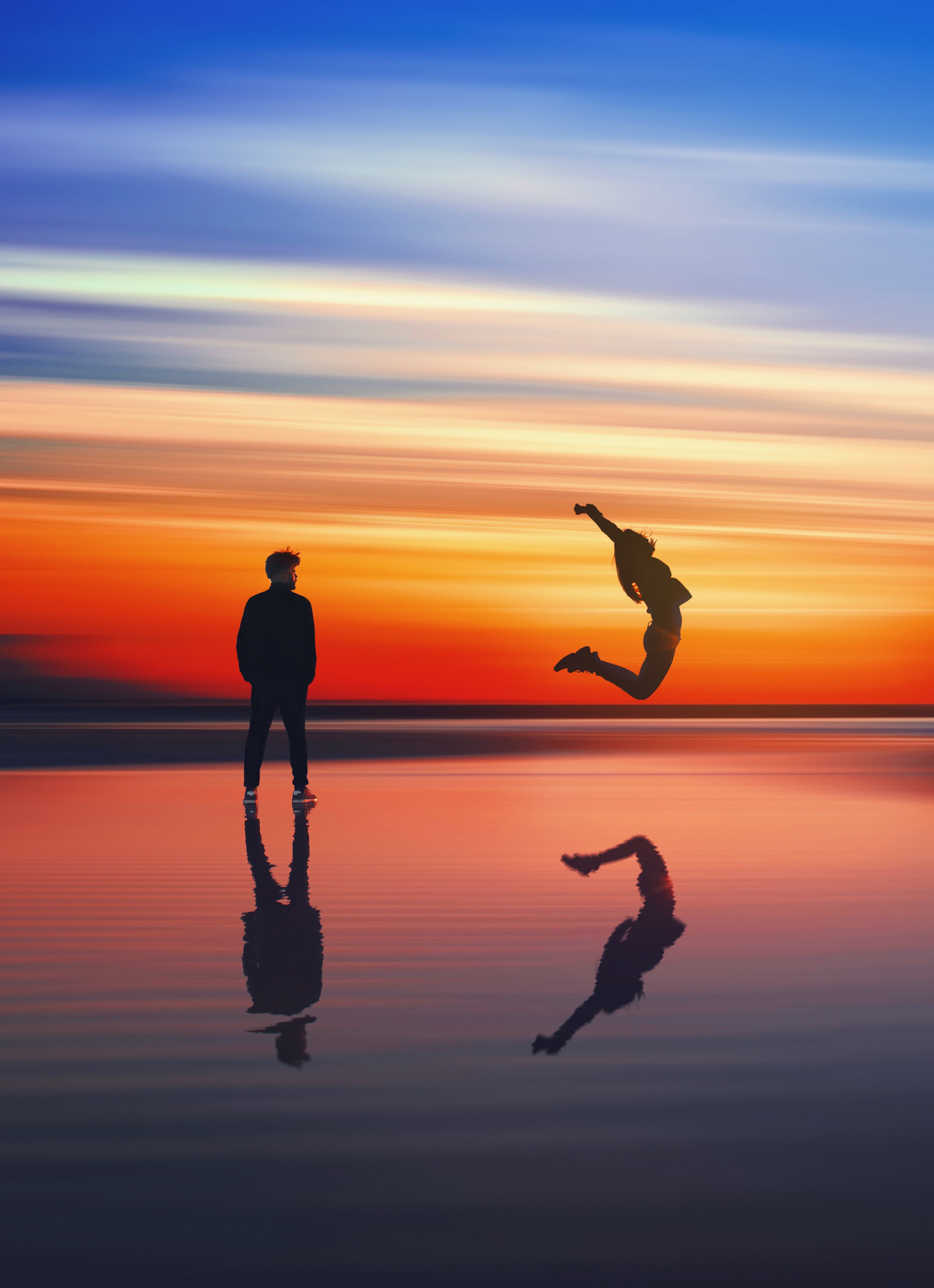 Photo of two people at the ocean at sunset with their silhouettes reflecting in the water