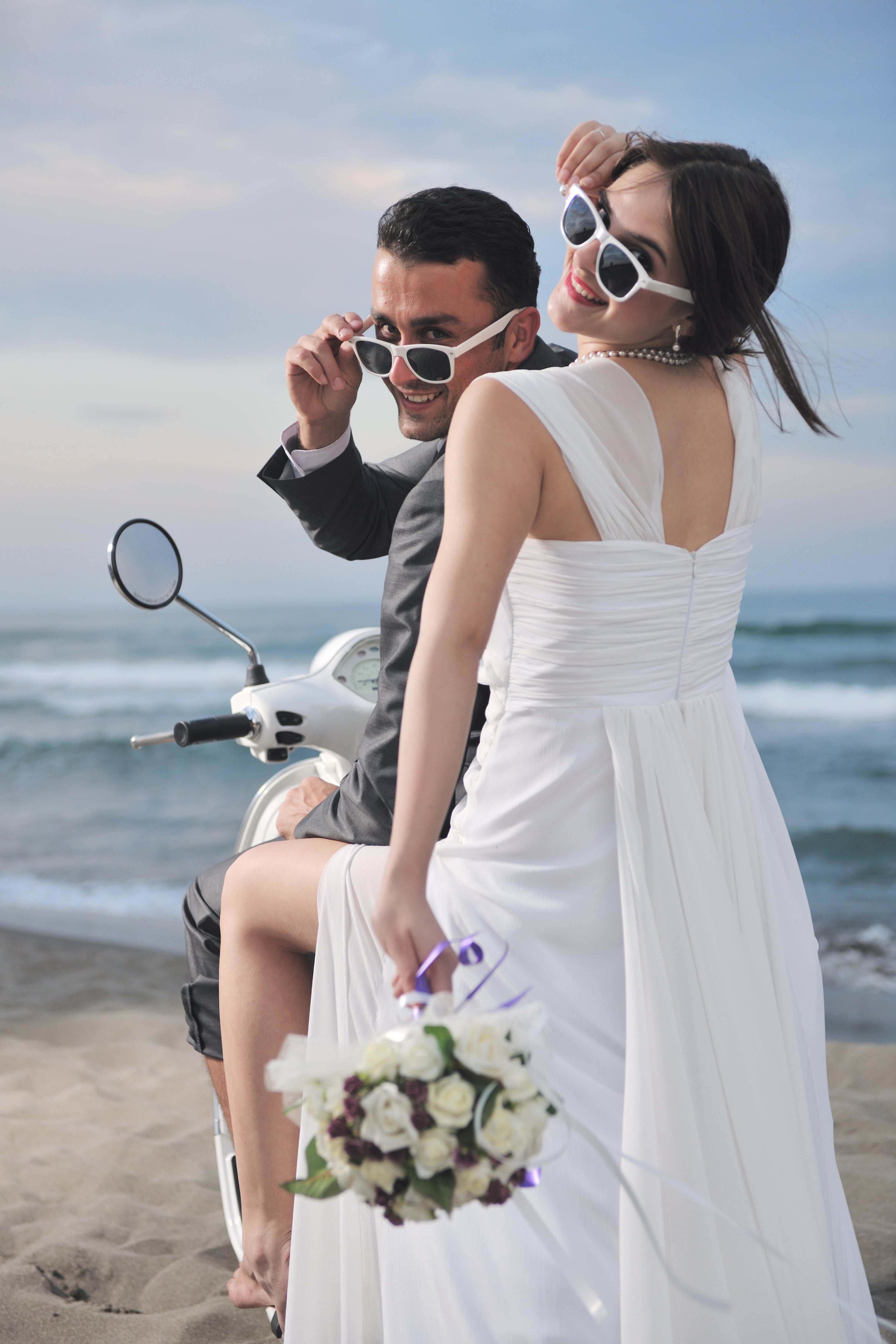 Just married couple wearing sunglasses on the beach having fun riding a scooter