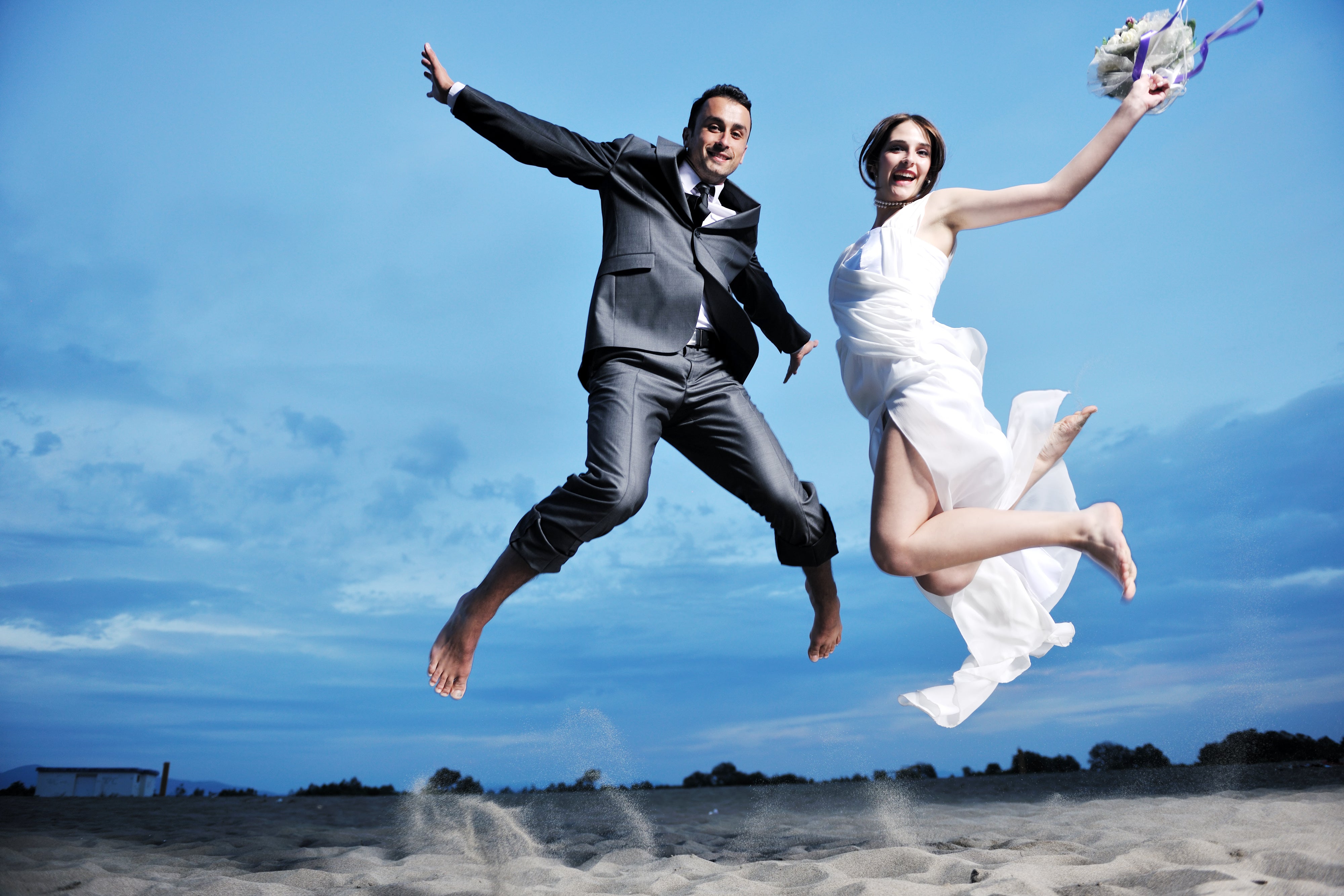 Bride and groom having fun jumping in the air at the beach