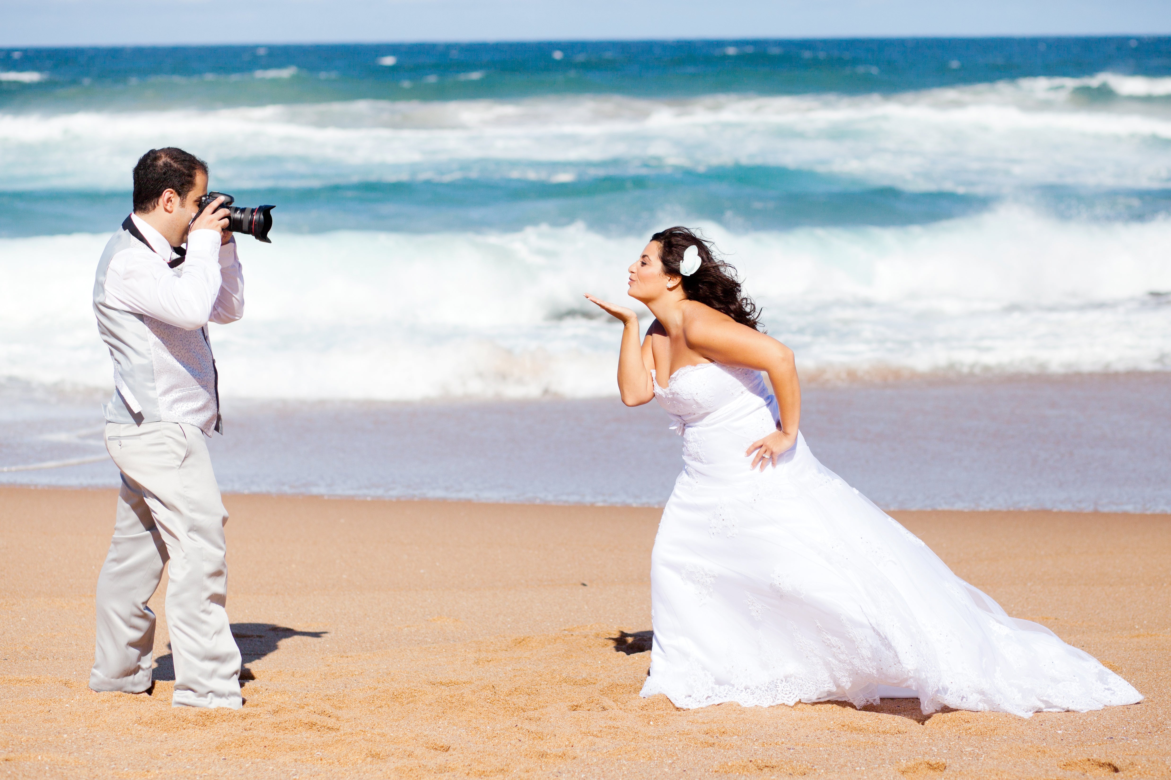 Photographer capturing a photo of the bride blowing him a kiss on the beach