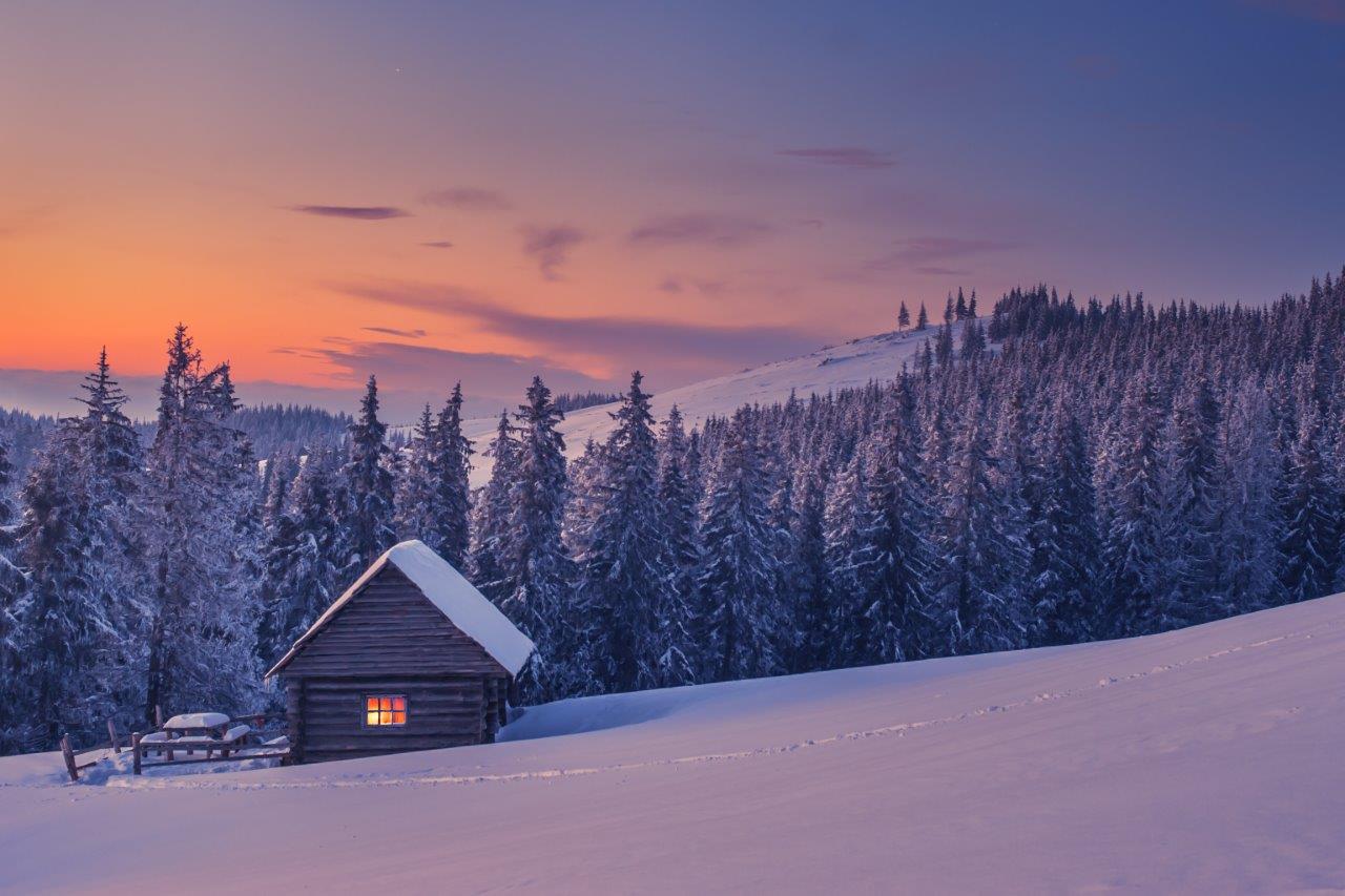 Snow-covered cabin in the mountains at dusk