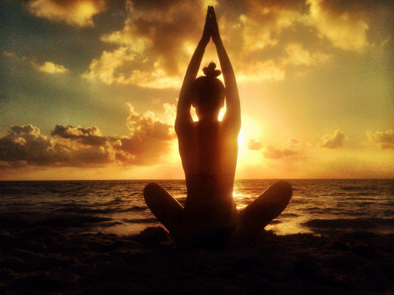 Silhouette of a person doing yoga on the beach at sunrise or sunset