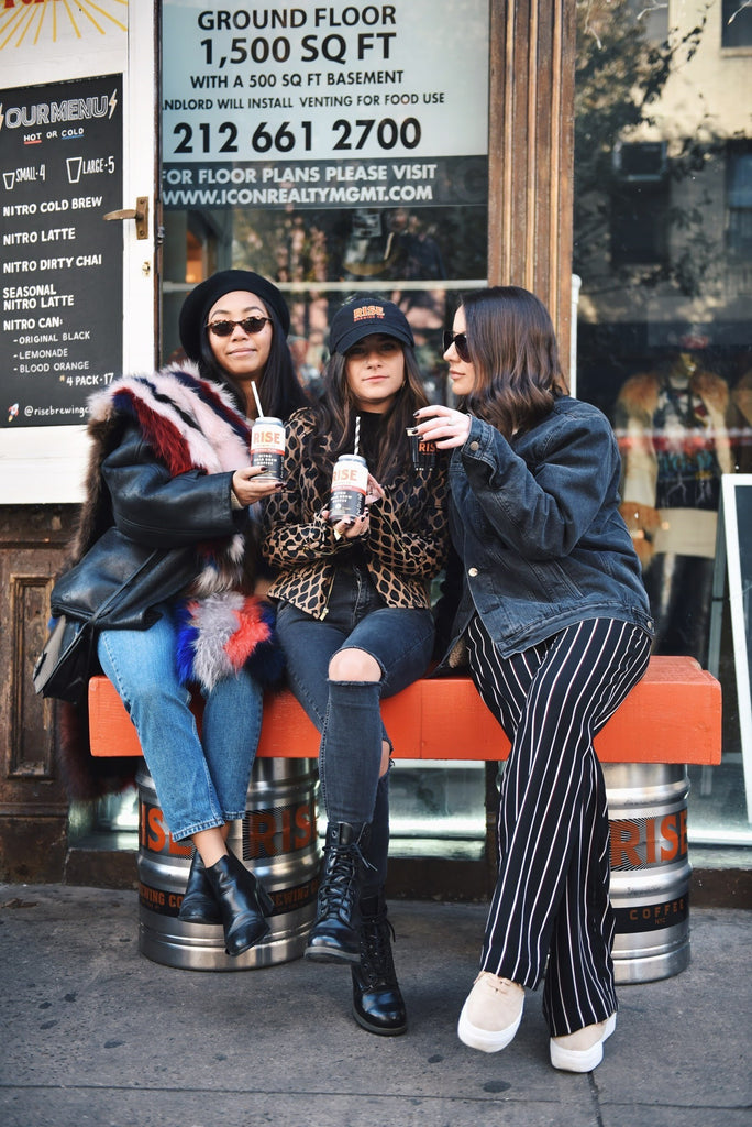 Women in front of RISE coffee cafe holding cans of RISE nitro cold brew coffee - RISE Brewing Co.