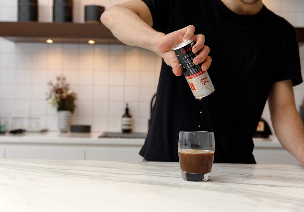 Man pouring can of RISE Original Black nitro cold brew coffee into glass in kitchen - RISE Brewing Co.