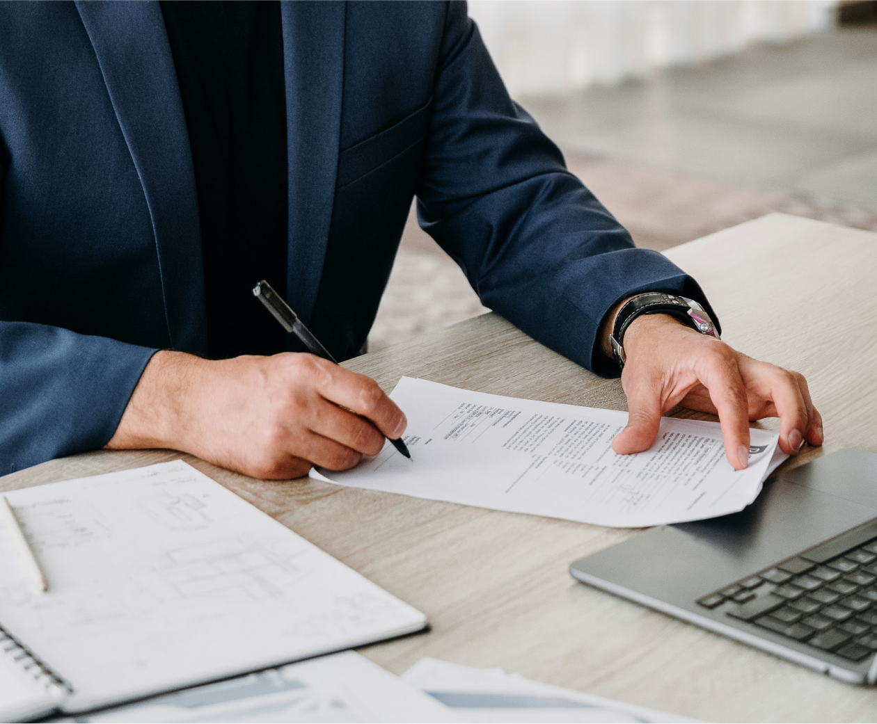 A white male entrepreneur reviewing and signing financial documents while sitting at his desk.