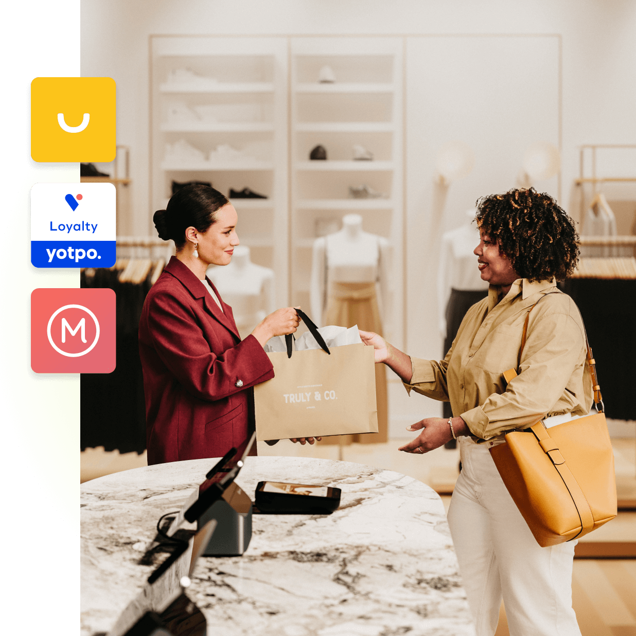 An elegant sales associate from Truly and Co hands a shopping bag to a chic customer. The two women are standing close to the checkout counter in a bright and beautifully-lit mall store. To the left of the image are icons for various clienteling apps available in the Shopify app store.