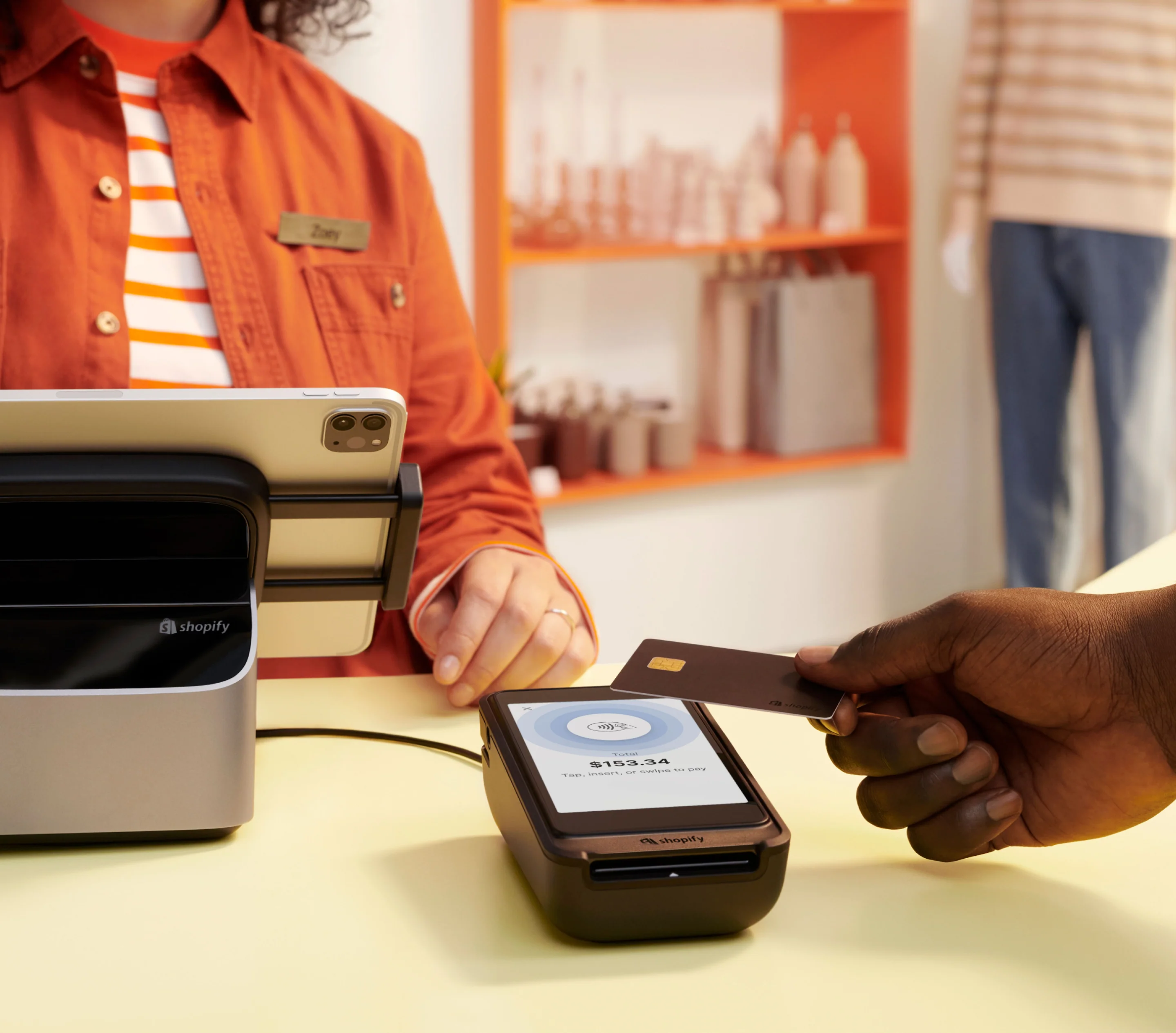 A sales associate waits behind the counter while a customer taps their credit card to pay on POS Terminal.