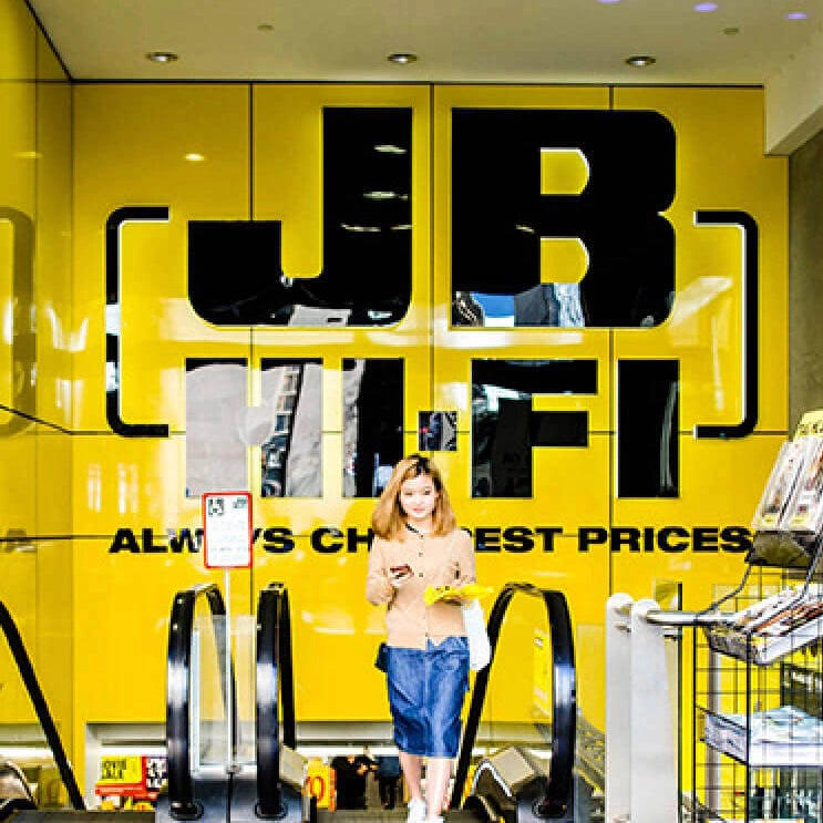 Woman coming up escalator in front of JB Hi-Fi store