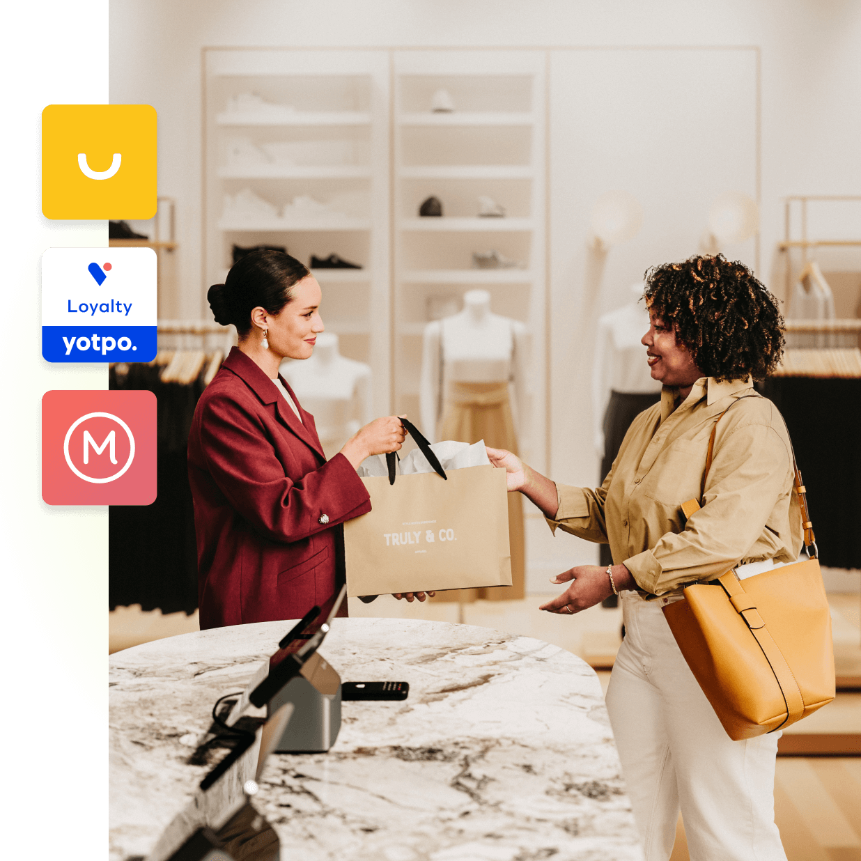 Eine elegante Verkaufskraft von Truly and Co überreicht einer schicken Kundin eine Einkaufstasche. Die beiden Frauen stehen in der Nähe des Kassenbereichs in einem hellen und schön beleuchteten Geschäft in einem Einkaufszentrum. Auf der linken Seite des Bildes sind Symbole für verschiedene Clienteling-Apps zu sehen, die im Shopify App Store erhältlich sind.