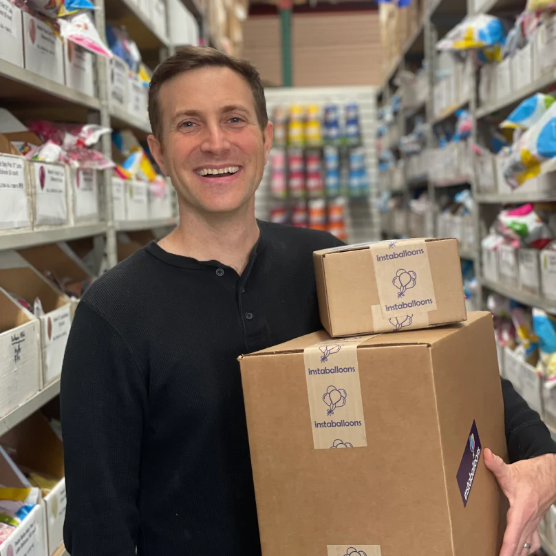 Jason Handman, CEO de instaballoons Wholesale, en una sala de envíos sosteniendo dos cajas