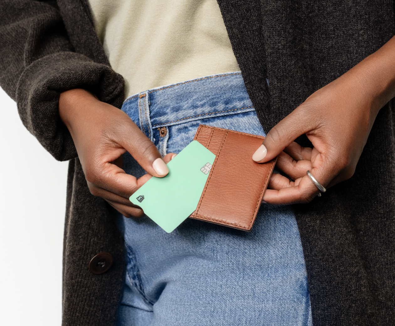 A Black woman puts her Shopify Credit business card back into her brown leather wallet