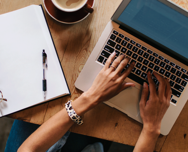 A merchant typing on their laptop with a notebook open next to them