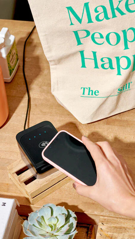 Foto de un cliente en la tienda de plantas The Sill mientras paga su compra tocando el hardware de Shopify con su teléfono