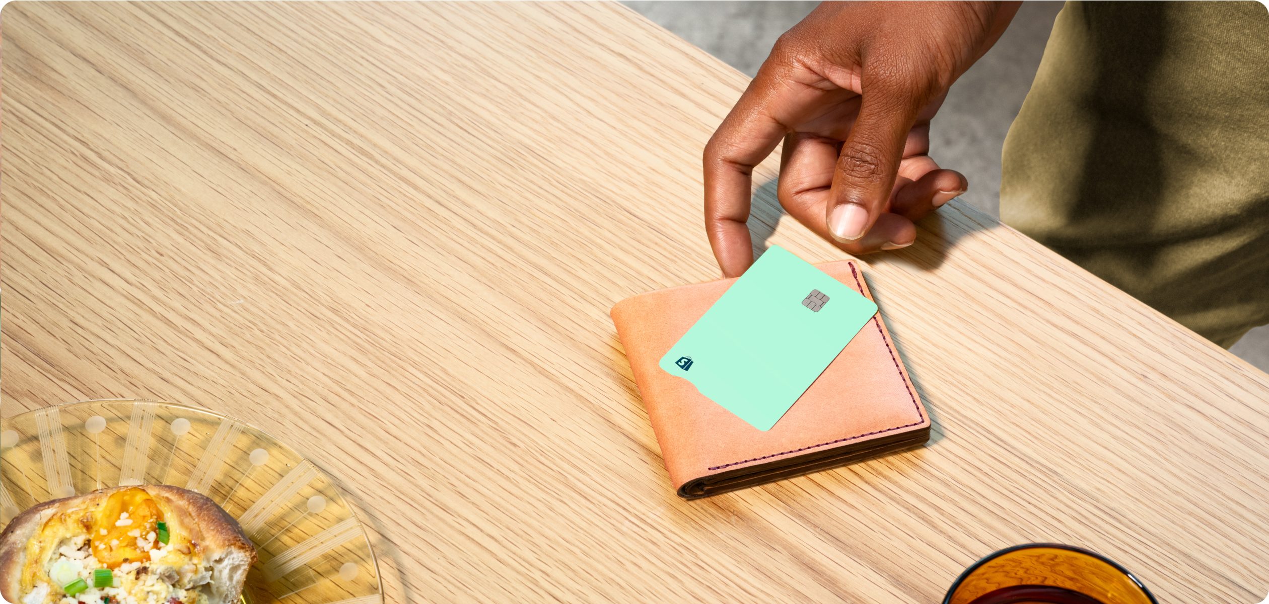 A Black man’s hand reaching for his Shopify Credit business card from his brown leather wallet